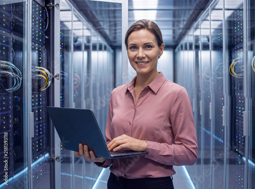 Cheerful female IT engineer holding laptop and smiling in modern server room data center