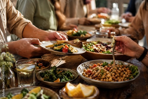 A group of people enjoying a healthy and delicious plant-based meal together at a wooden table, with various dishes of vegetables, legumes, and grains.