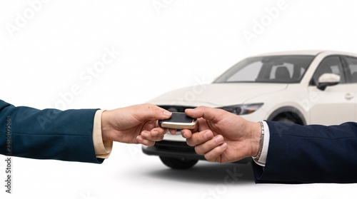 Handover of a car key between two people in business attire with a white car in the background
