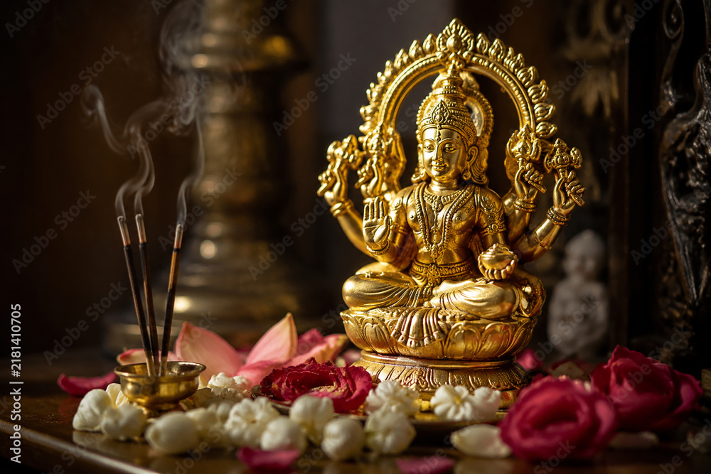 Obraz premium A small gold-plated statue on an altar with flower petals and incense sticks.