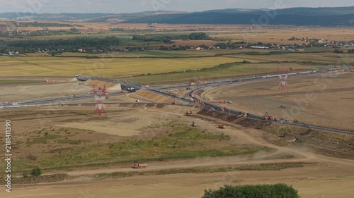 Aerial panoramic view of Autostrada Moldovei A7 Nod Bacau construction site with heavy machinery, highway interchange, and rural landscape in warm sunlight. 4K video.