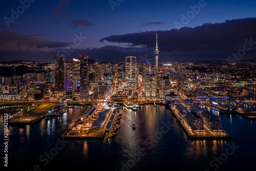 Картината върху платно Illuminated Auckland city skyline and iconic Sky Tower glowing at night above the busy waterfront harbor in Auckland, New Zealand