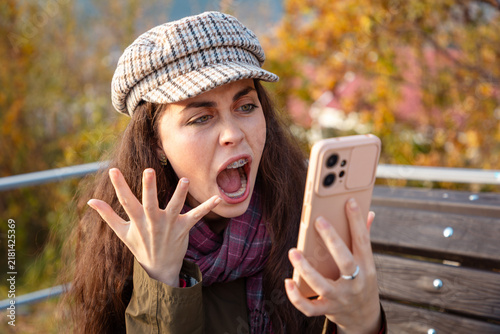 Cuadro en lienzo Young Caucasian woman holding smartphone and shouting in anger after reading unexpected online news