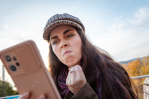 Fotografía Female holding mobile phone and reacting aggressively to unexpected online content