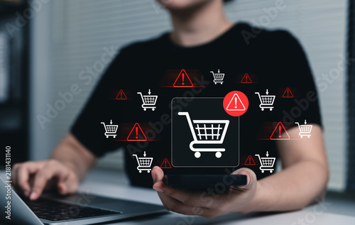 Naklejka E-Commerce Warning and Shopping Cart Risk Concept. Woman using laptop and smartphone with shopping cart icons, online purchase issues, checkout risk, transaction warning, e-commerce security concerns