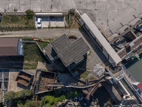 Aerial view of the dam and weir structure on the Po River, featuring concrete infrastructure, a small building, and surrounding riverbanks in San Mauro Torinese, Piedmont, Italy.
