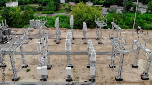 Aerial drone view of an electrical substation under construction in Sumy, Ukraine. High-voltage transformers, switchgear, transmission equipment, utility buildings, workers, and a yellow excavator