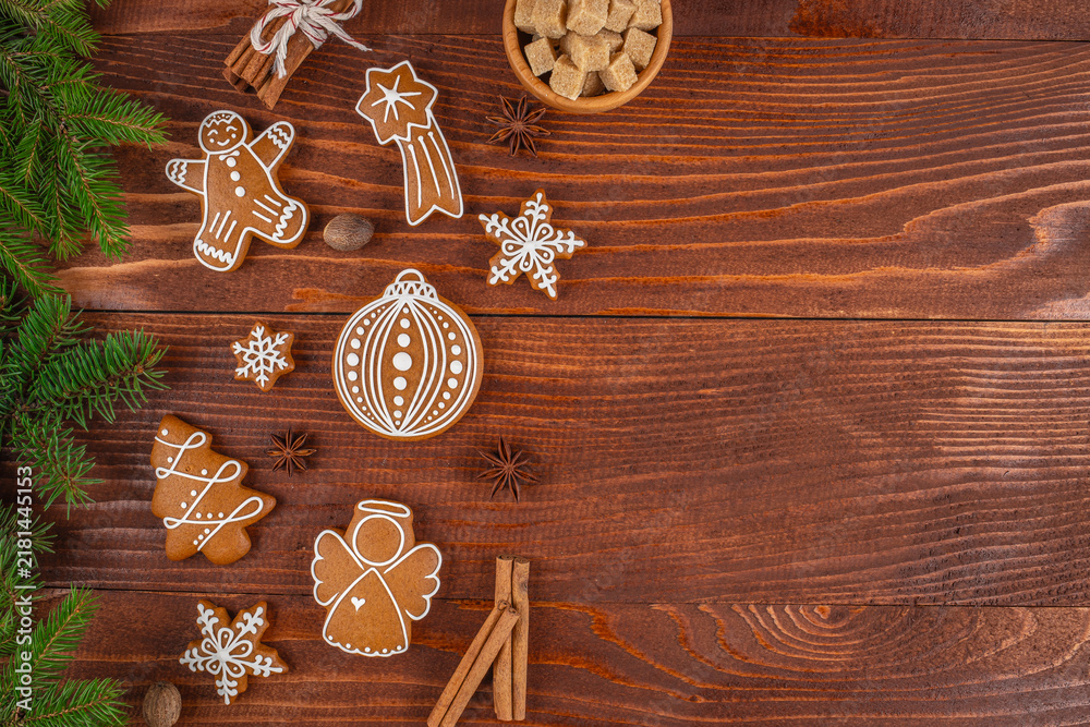 Fototapeta premium Gingerbread cookies shaped like a man, angel, and ornament arranged on a wooden table with cinnamon sticks, sugar cubes, and pine branches for a festive holiday setting