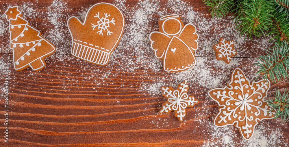 Fototapeta premium Gingerbread cookies shaped like Christmas tree, mitten, angel, snowflake, and star arranged on wooden table with powdered sugar and pine branches