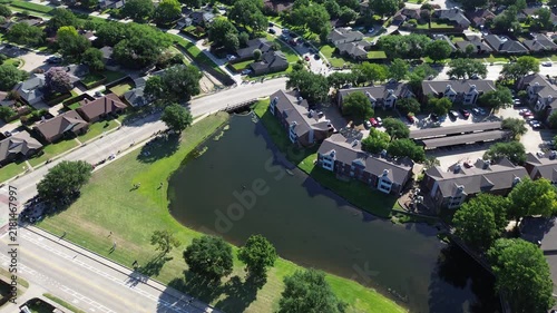 Reflective retention ponds flank Parkway Boulevard at Moore Road pedestrian crossings. Manicured grass slopes, brick apartment terraces, paved parking bays define scenic Coppell, Texas.
