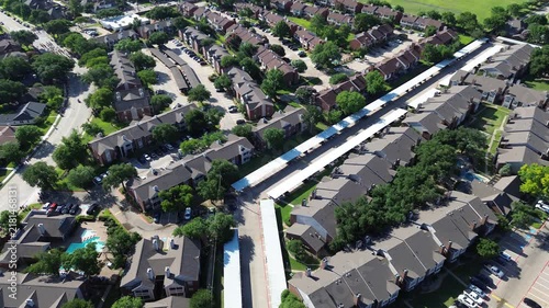 Sprawling residential apartment properties line Parkway Boulevard near Mockingbird Lane. Parallel white parking canopies, shimmering community swimming pools, shady trees fill Coppell, Texas.