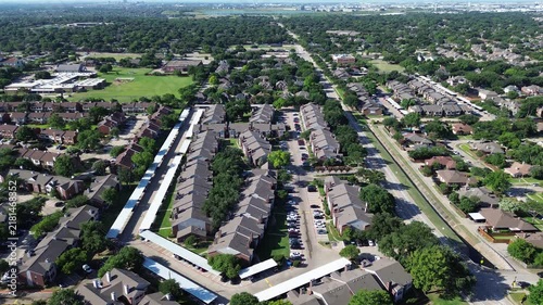 Multifamily residential buildings align beside Parkway Boulevard near Mockingbird Elementary School. White covered carports, paved parking courts, lush mature trees populate Coppell, Texas.