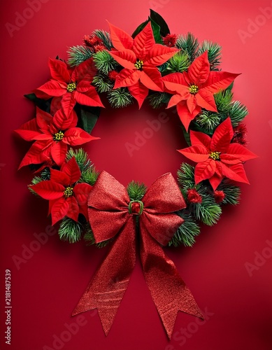 Poinsettia flowers wreath with red velvet bow on red background. Christmas concept