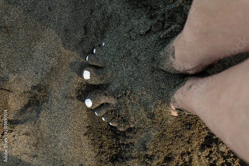 Konstfotografi A person stands barefoot on wet dark volcanic sand along a tropical beach in Costa Rica