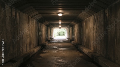 Long Concrete Underpass Tunnel Leading Toward Bright Daylight Exit with Industrial Lighting Fixtures Mounted on Ceiling