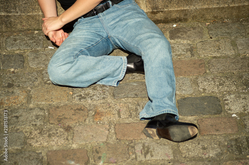 Foto A person wearing blue jeans and black boots lies or sits on a cobblestone street in Paris, France