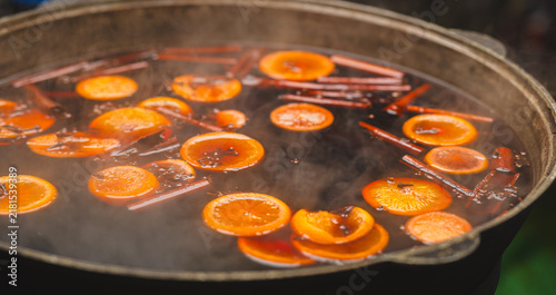Cuadro en lienzo Mulled wine with orange slices and cinnamon sticks cooking in large pot at street market
