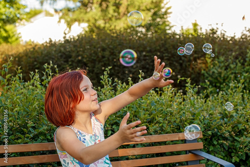 A portrait of a sweet girl playing with soap bubbles in a public park.