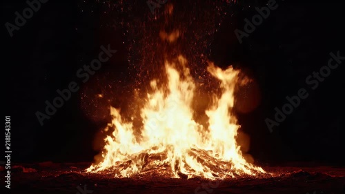 A massive realistic fire blazing against an infinite pitch-black background. Tall flames rise dramatically from the bottom center of the frame, continuously dancing, twisting, splitting, and merging w