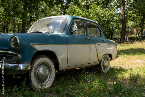 Фотография Old blue and white retro automobile with chrome bumper and white wall tires stands on grass in sunny summer park