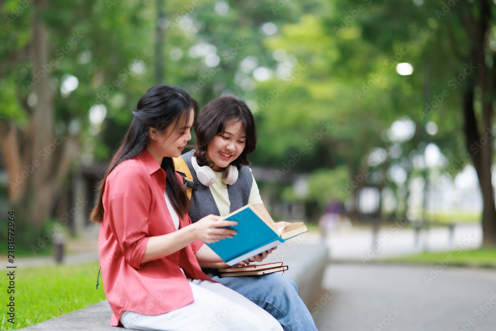 Fototapeta premium Two university students learning together outdoors, sharing a textbook and smiling, engaging in educational discussion and collaborative study on campus