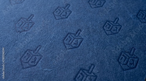 A blue textured surface features a repeating pattern of dreidels, evoking a sense of Hanukkah tradition and festive celebration.