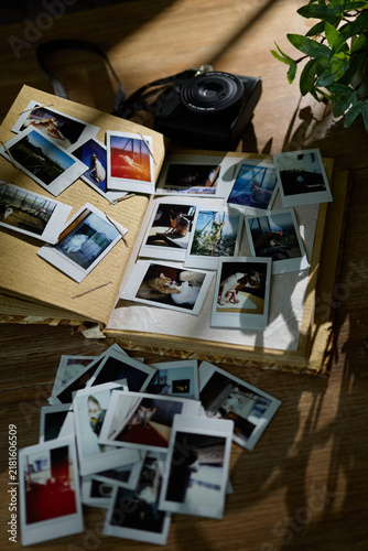 Old photo album with instant pictures and camera on wooden table