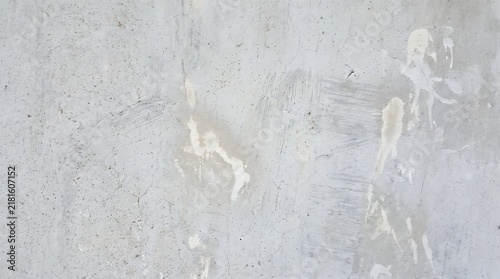 Weathered light gray concrete wall surface featuring unique cracked patterns and worn white paint drips providing a vintage industrial texture