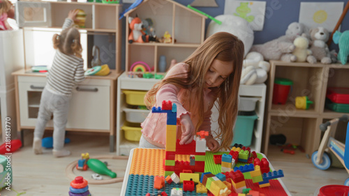 Fotografie Two girls stacking plastic toy blocks at a small table in a colorful playroom inside a building; concentration and cooperation