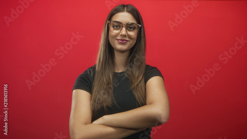 Fotografie Woman with glasses crossing her arms and smiling against a red studio backdrop; confidence approachable