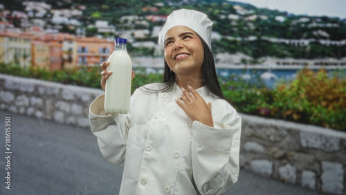 фотографія Woman chef holds a milk bottle in one hand and gestures palm up while smiling on street; pride craft