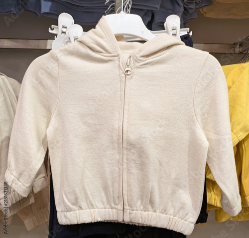Tiempo de otoño. Vista de frente de una sudadera infantil con capucha y cremallera de color blanco colgada de una percha en una tienda 