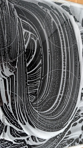 Abstract pattern of white soap suds and streaks forming intricate, dynamic swirls and lines on a dark, reflective surface, creating a vibrant, textured background ideal for cleaning,