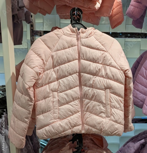 Tiempo de otoño. Vista de frente de una chaqueta acolchada infantil con cremallera de color rosa colgada en una tienda de ropa