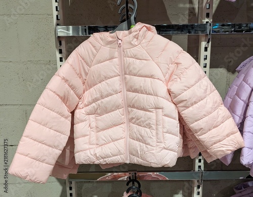 Tiempo de otoño. Vista de frente de una chaqueta acolchada infantil con cremallera y capucha de color rosa colgada en una tienda de ropa