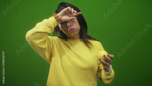 Canvas Print Woman holding lemon with hand over eyes and puckered mouth, wearing yellow sweater in studio; weariness reluctance