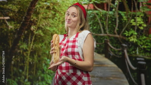 Bild auf Leinwand Woman chef holding a baguette with hands presented on a wooden bridge in forest; cheerful homestyle warmth