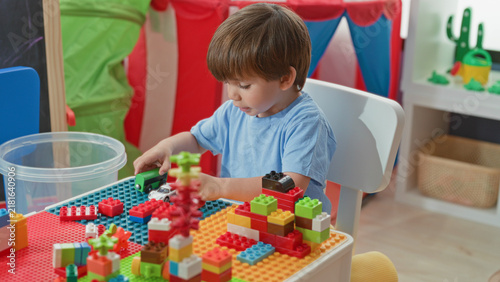 Принти на полотні Boy playing with blocks and toy car, hands manipulating bricks at a playroom table inside a building; concentration