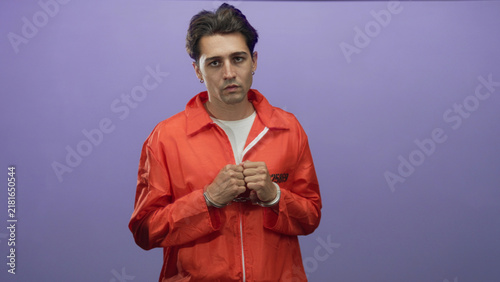 Foto Man prisoner in orange jumpsuit with handcuffs clasping hands in front, facing purple studio backdrop; remorse solitude