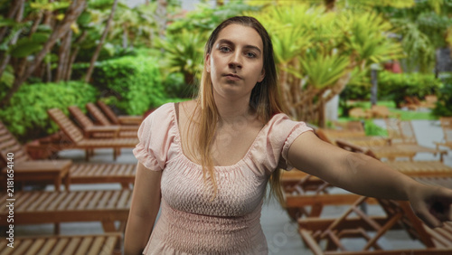 Fotografie Woman hispanic pointing arm toward lounge chair and pool deck in building wearing pink dress and neutral expression; determination