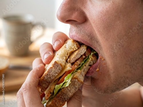 Close-up of a Young Man Enjoying a Healthy Whole Grain Sandwich During a Nutritious Midday Break in a Bright Kitchen Setting