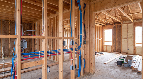 Residential house construction site interior featuring wood wall framing, electrical wiring conduits, and junction boxes during the rough-in stage.