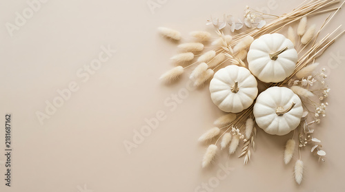 Three decorative white pumpkins arranged with dried bunny tail grass on a neutral beige background fall decor autumn background harvest season