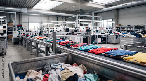 Clothing sorting conveyor in textile recycling factory warehouse with workers folding and inspecting garments