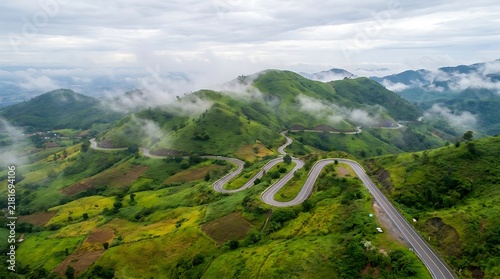 Winding asphalt road through lush green mountains in cloudy weather