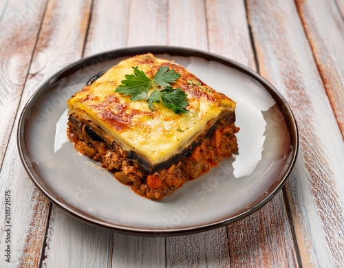 a delicious portion of traditional greek moussaka with eggplant and meat sauce on a rustic white wood surface