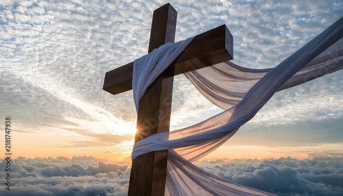 Wooden cross with white cloth against dramatic sky and clouds at sunrise.