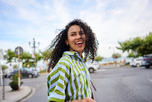 Young woman with curly hair smiling on urban street