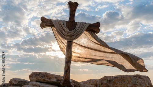 Wooden cross draped with cloth on rocks with clouds and sun rays.