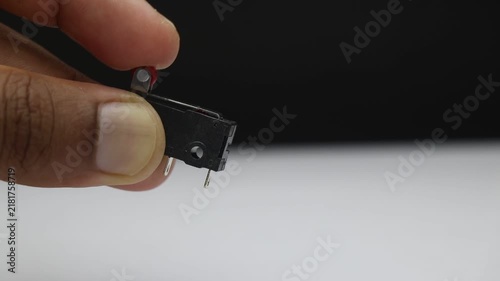 Limit switch electromechanical component held in fingers showing the small lever and metal pin that trips when pressed against an object